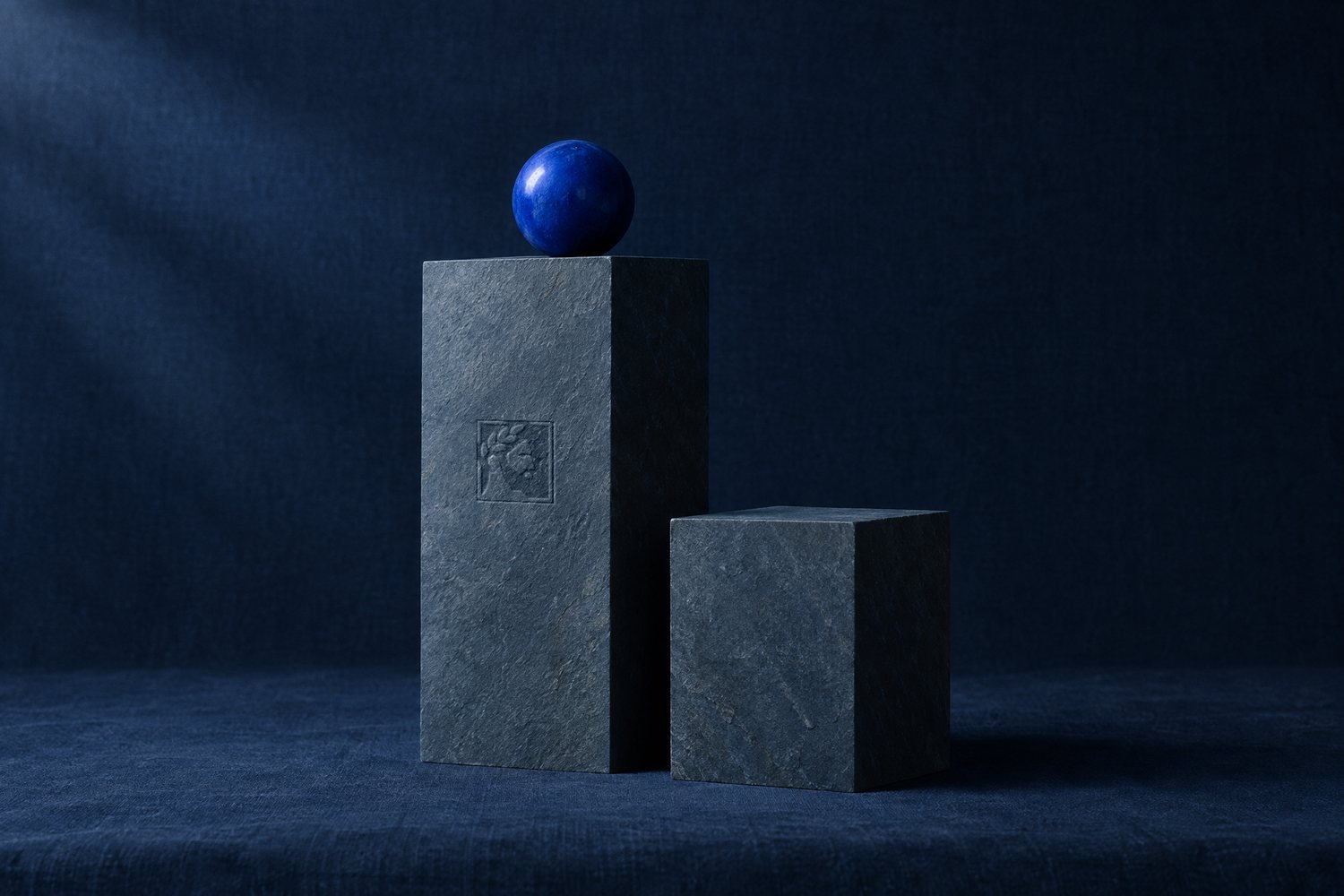 Two slate stone plinths of different heights with a cobalt sphere on the taller one, the Olivent mark pressed into its face