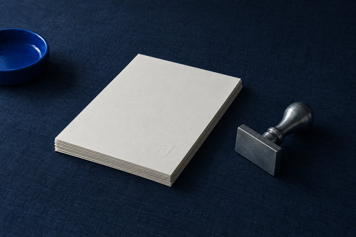 A stack of blank cream paper beside a steel desk stamp, the Olivent mark embossed in the top sheet
