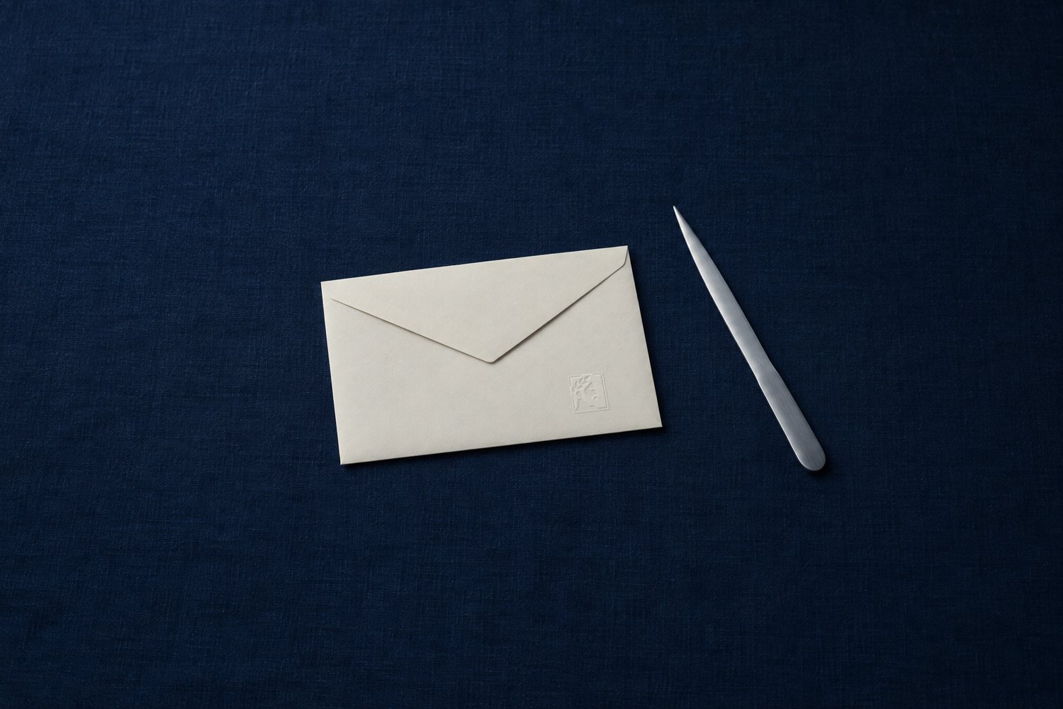 A sealed cream envelope with a steel letter opener beside it, the Olivent mark embossed on the envelope