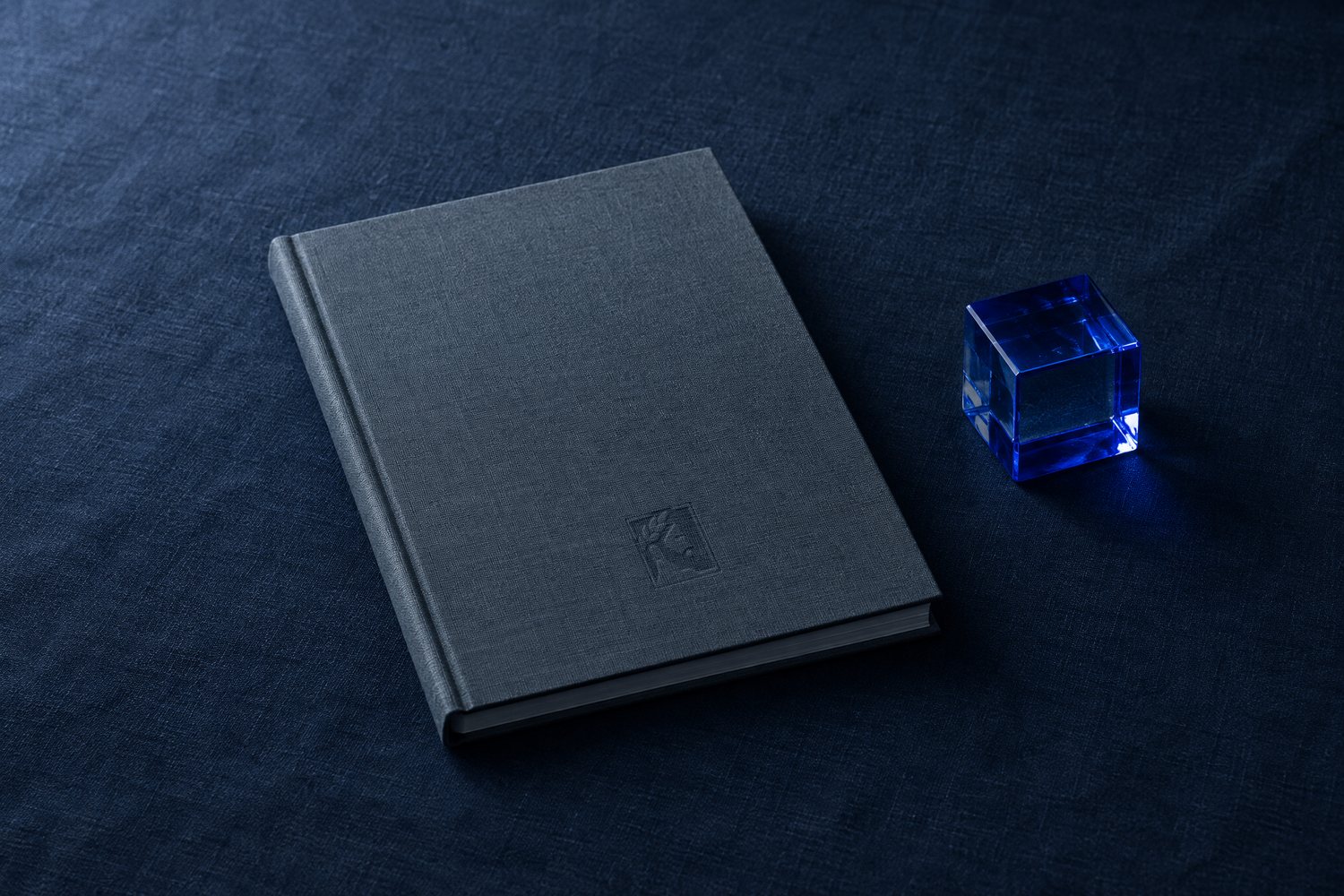 A slate-grey clothbound report with a cobalt glass cube beside it, the Olivent mark pressed into the cover