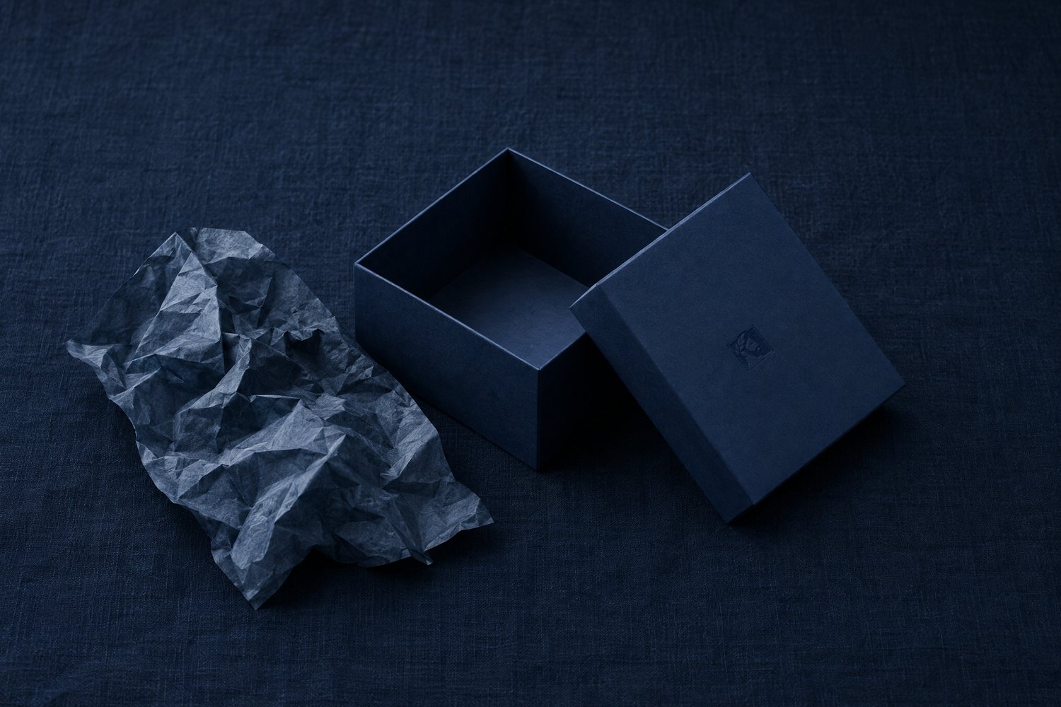 An empty navy box with its lid set beside it, the Olivent mark pressed into the lid, crumpled wrapping paper nearby