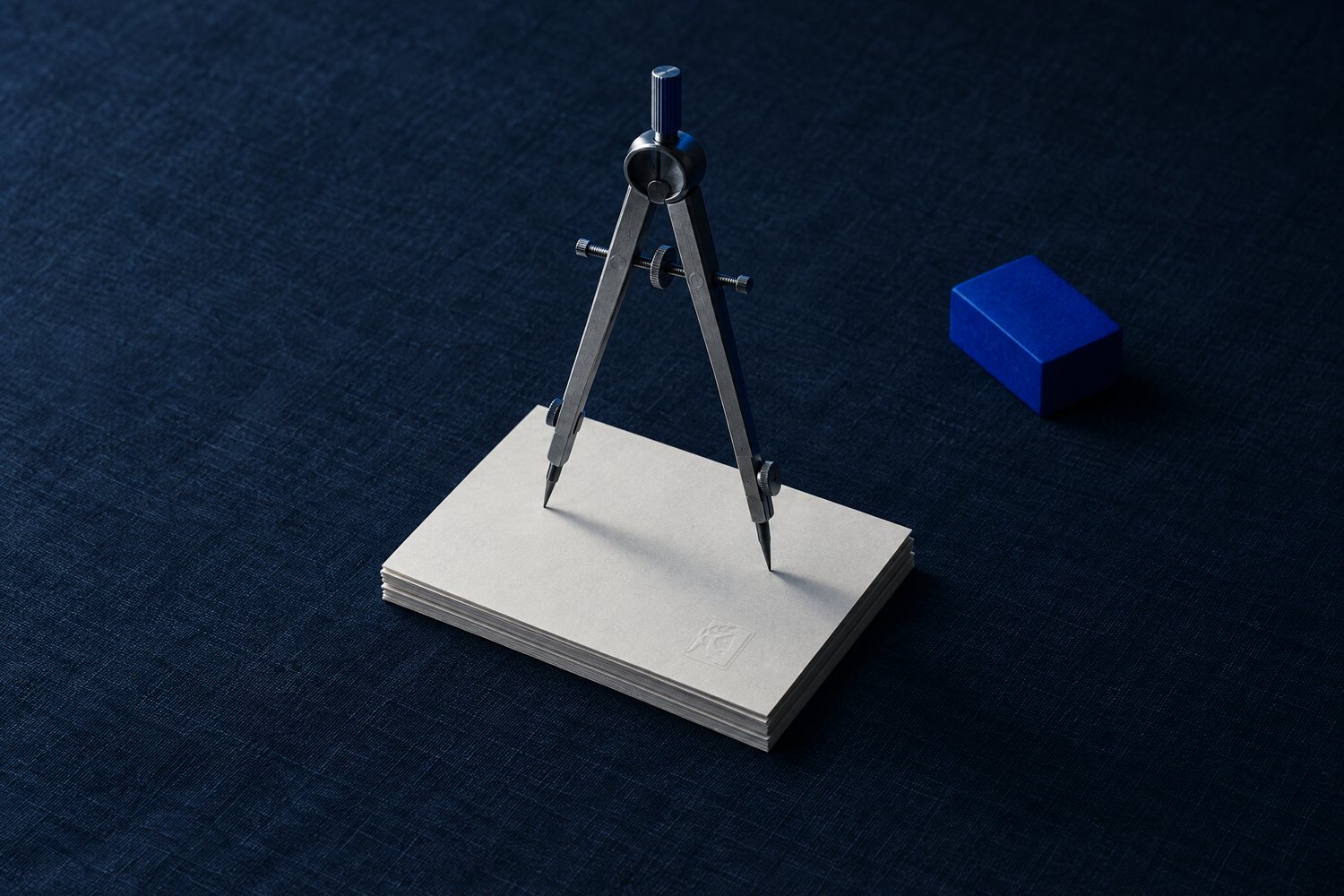 A steel drafting compass standing on a stack of blank cards, the top card embossed with the Olivent mark