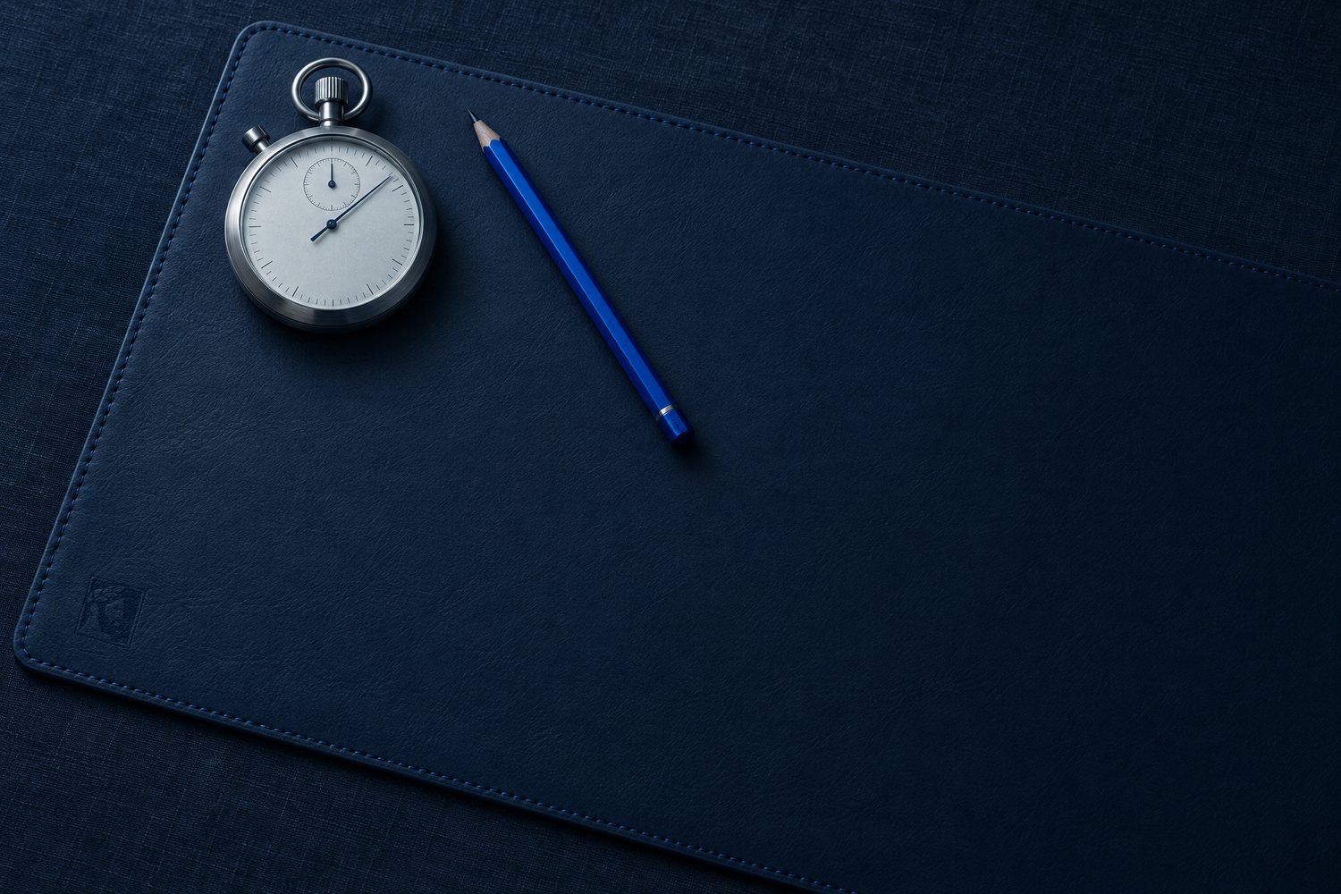 A steel stopwatch and a cobalt pencil on a navy leather desk mat, the Olivent mark pressed into its corner