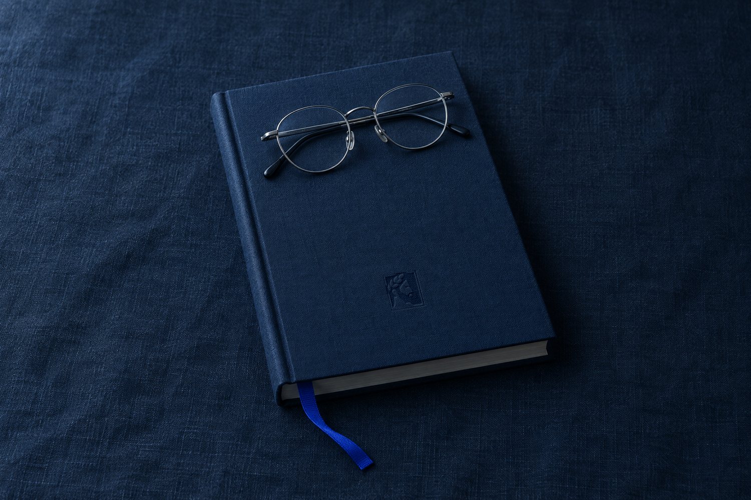 A navy hardcover book with steel-rimmed reading glasses on it, the Olivent mark pressed into the cover
