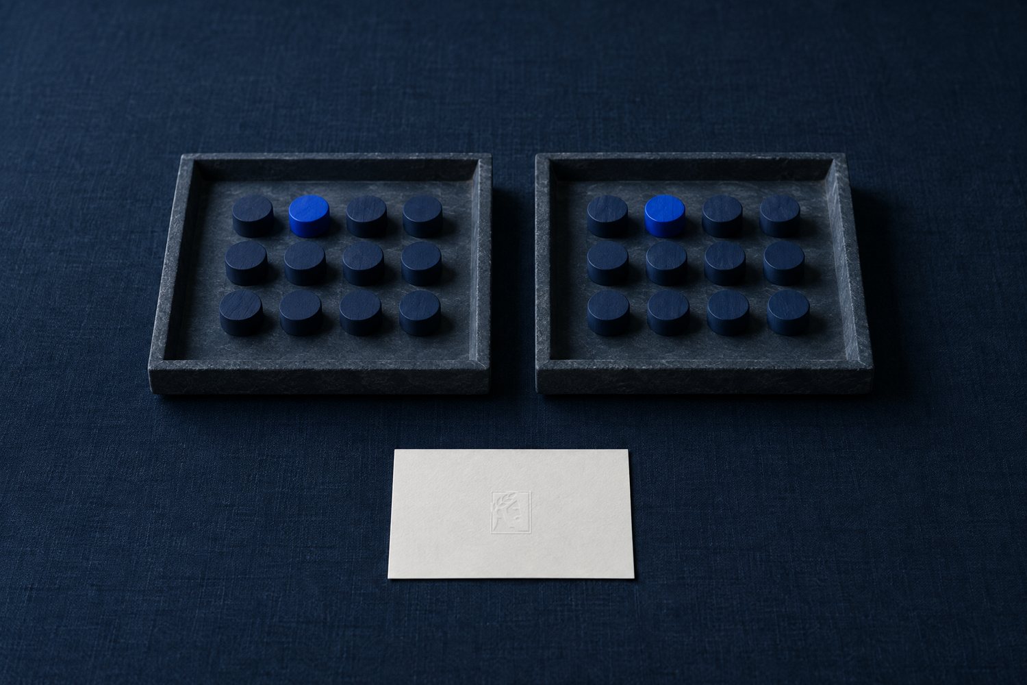 Two slate trays holding the same pattern of navy tokens with one cobalt token in the same spot, above a white card embossed with the Olivent mark