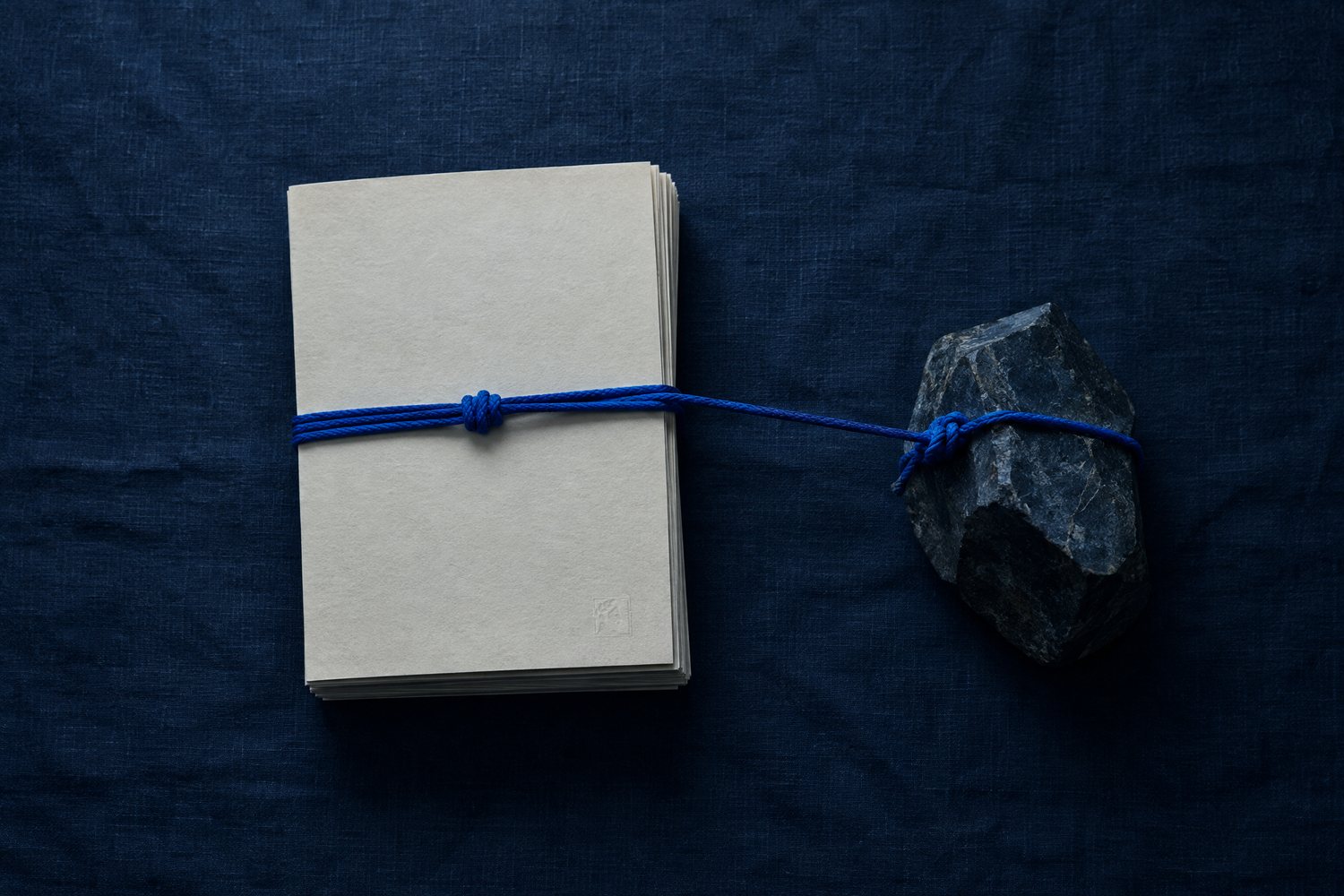 A cream document tied with a blue cord to a heavy stone