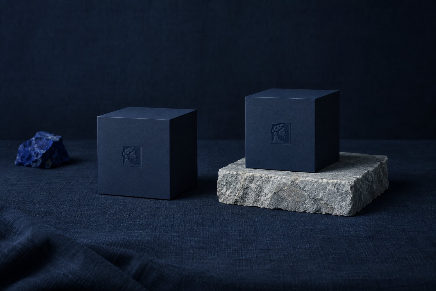 Two identical navy cubes, one on the linen and one on a slab of pale stone, both stamped with the Olivent mark