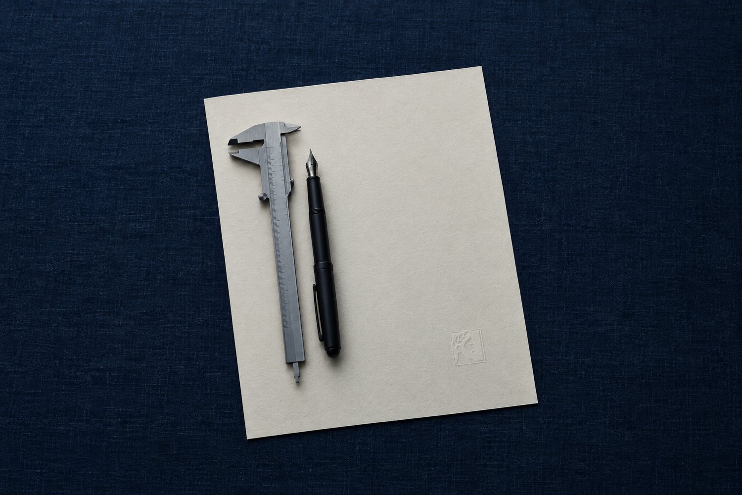 A sheet of cream paper with a steel caliper and a black fountain pen, the Olivent mark embossed in the lower corner