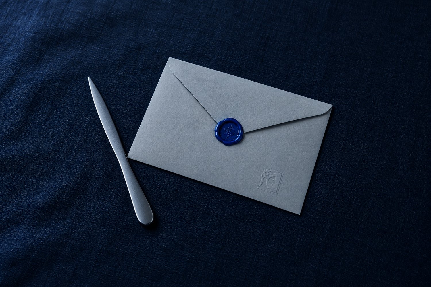 A grey envelope sealed with cobalt wax, the Olivent mark embossed in its corner, a steel letter opener beside it