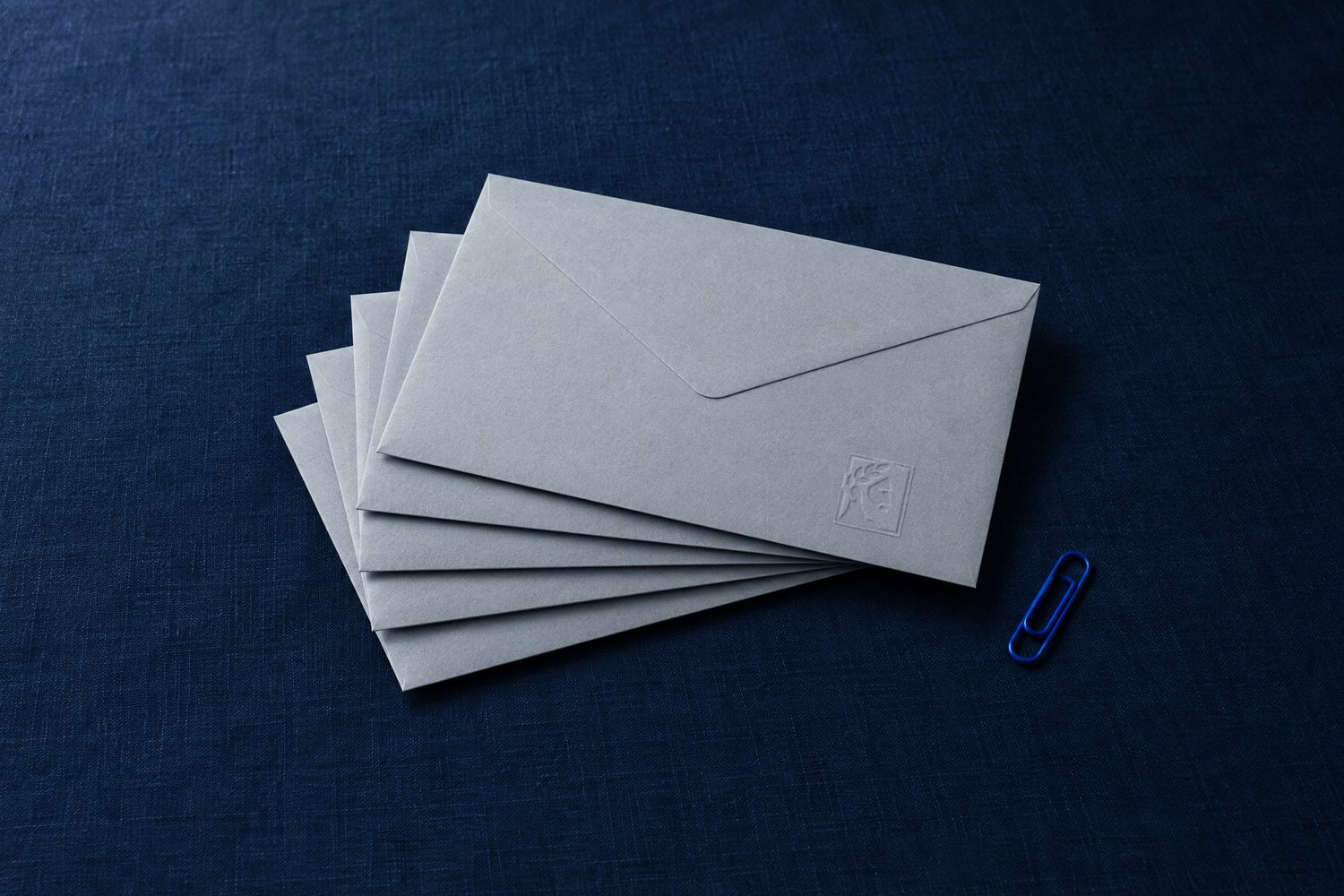 A fanned stack of grey envelopes, the top one embossed with the Olivent mark, and a cobalt paper clip