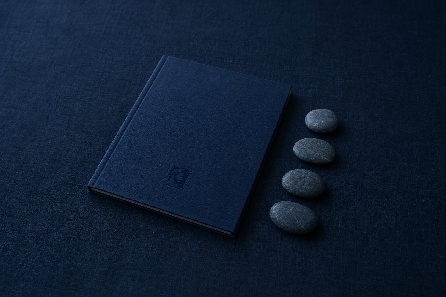 A closed navy cloth folder with the Olivent mark debossed on its cover, four slate pebbles lined up beside it