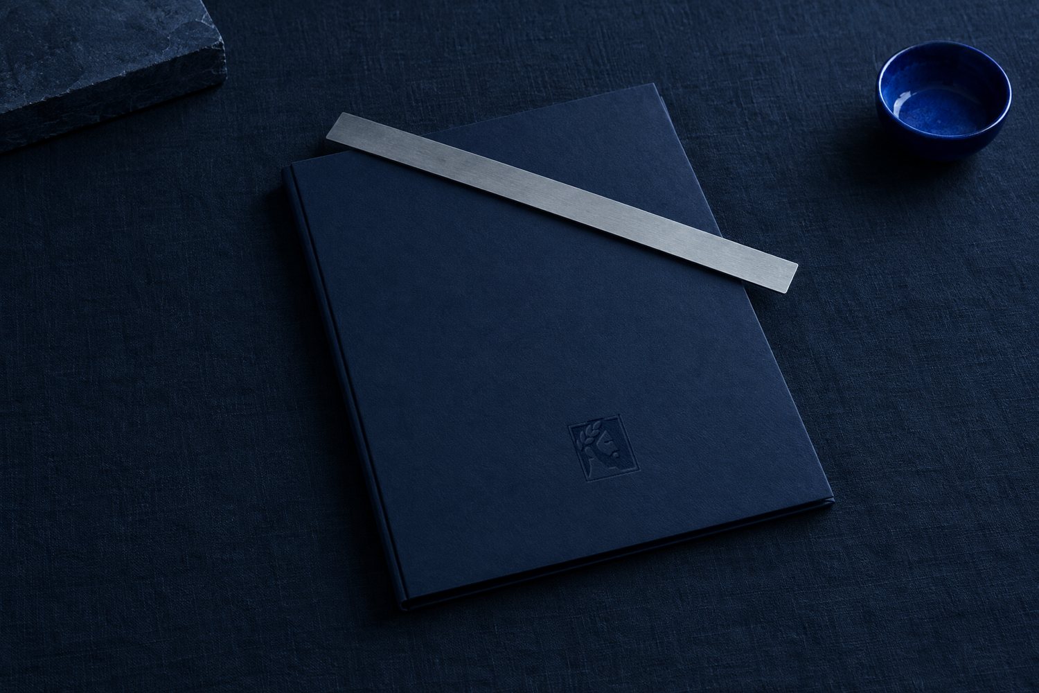 A steel ruler across a closed navy folder with the Olivent mark pressed into the cover
