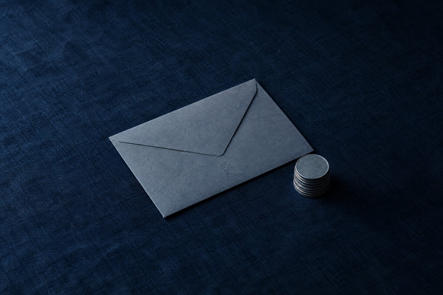 A slate envelope next to a short stack of steel coins, the Olivent mark embossed on the envelope